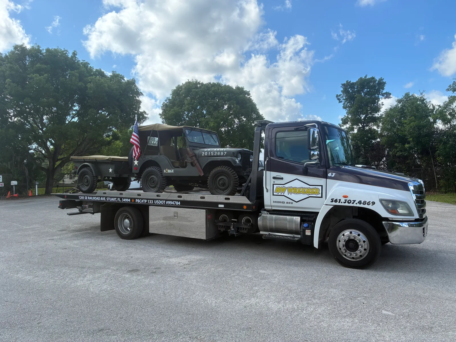 KW Wrecker Service flatbed transporting a vintage US Army Jeep with American flag flying
